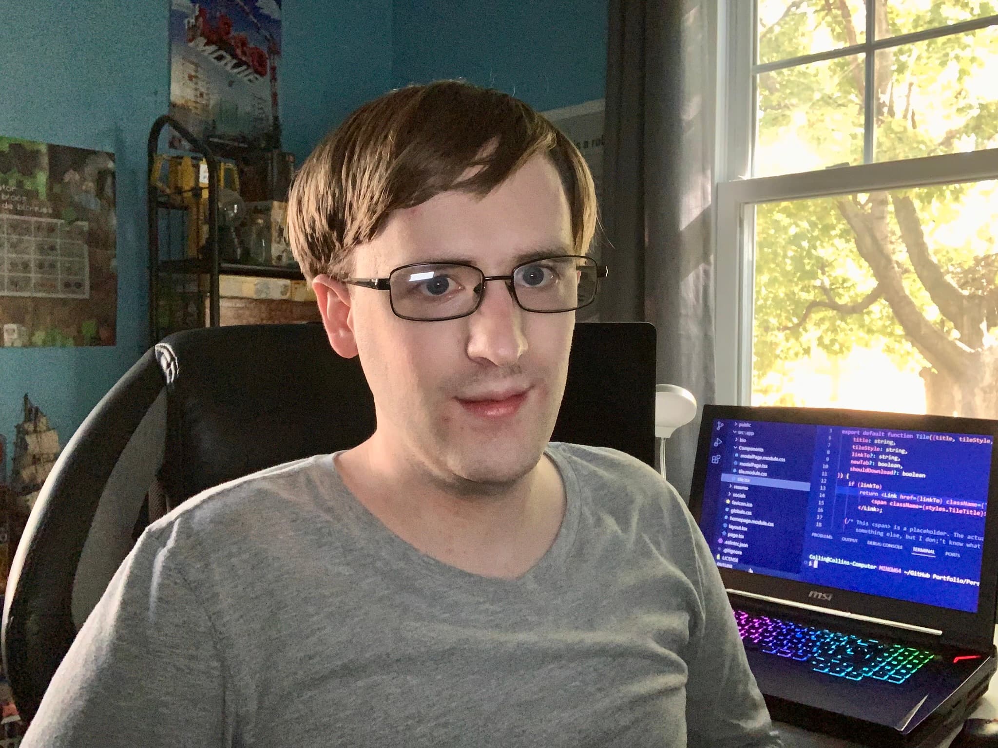 A picture of me sitting at my desk trying to look friendly. I have my computer open in the background with some of my code open.